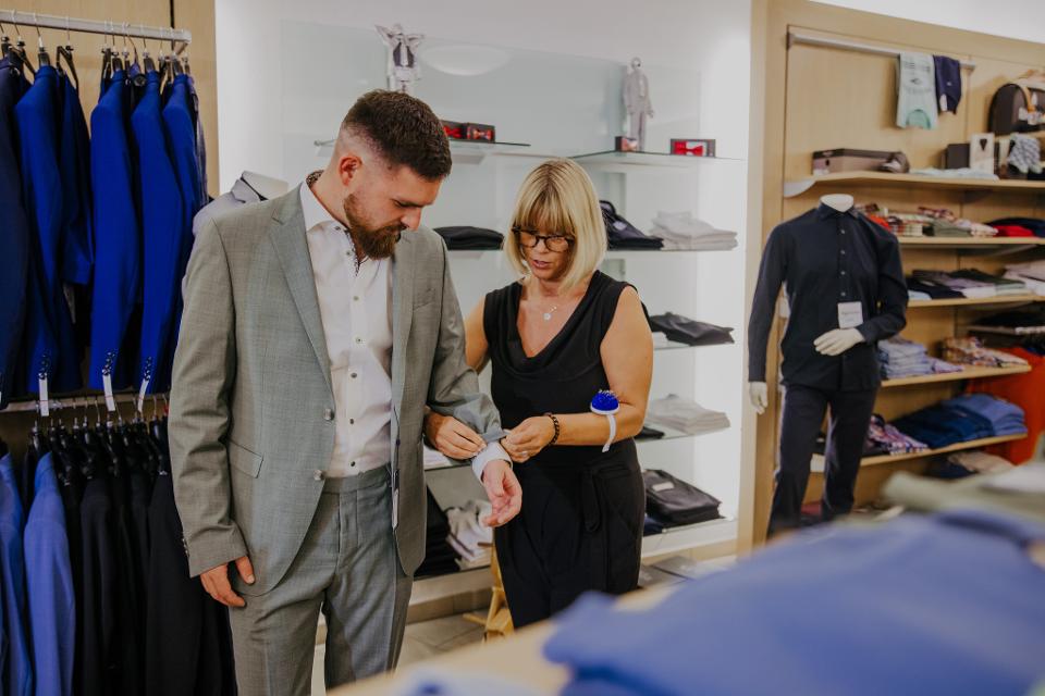 Mitarbeiterin steckt einem Kunden die Länge des Sakkoärmels ab für die Änderung beim Schneider.